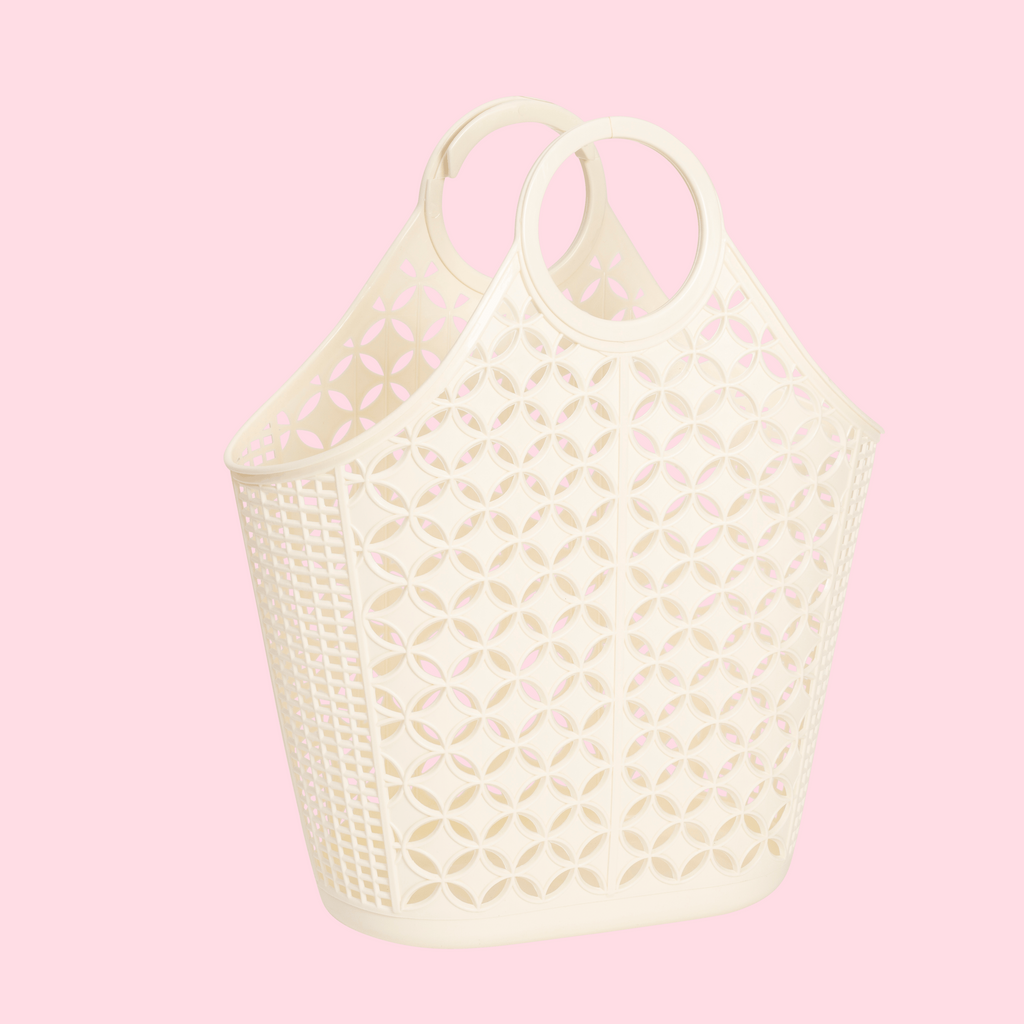 A cream-colored plastic basket bag with circular handles and a geometric cutout pattern, shown against a solid light pink background.