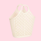 A cream-colored plastic basket bag with circular handles and a geometric cutout pattern, shown against a solid light pink background.