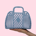 Blue woven handbag held by a hand against a pink background